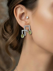 Close-up of a woman wearing diamond and peridot earrings with a blurred background