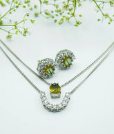A silver jewelry set including a necklace and earrings with pear-cut zultanite stones set in a half-flower design, with white zirconia sparkle, displayed on a white background with delicate flowers.