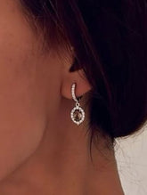 Close-up of a person wearing silver hoop earrings and a necklace with a white background