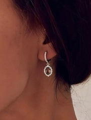 Close-up of a person wearing silver hoop earrings and a necklace with a white background